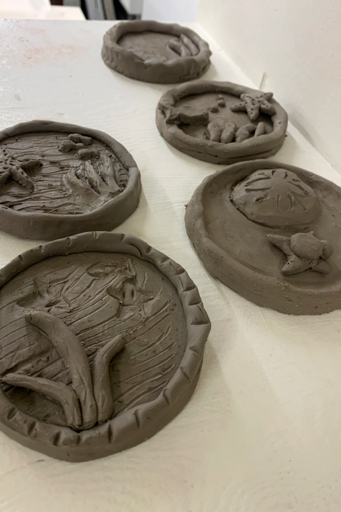 Clay circles shaped like portholes are filled with sculpted seaweed, sand dollars, and fish