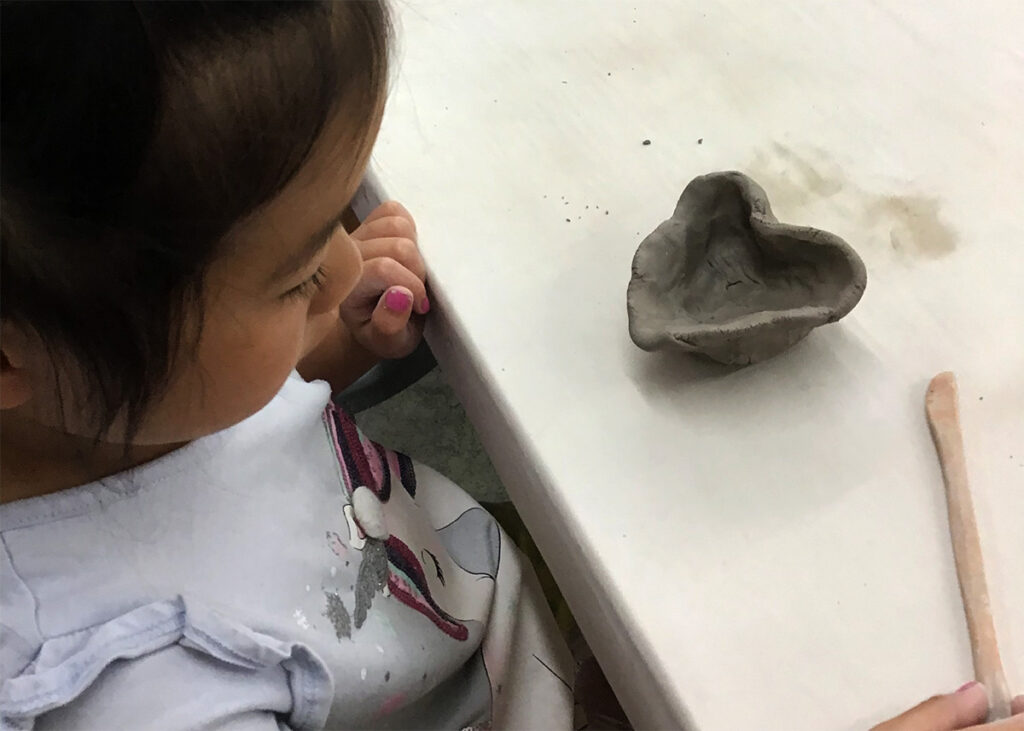 a young child looks down at the pinched pot they made in the shape of a heart.