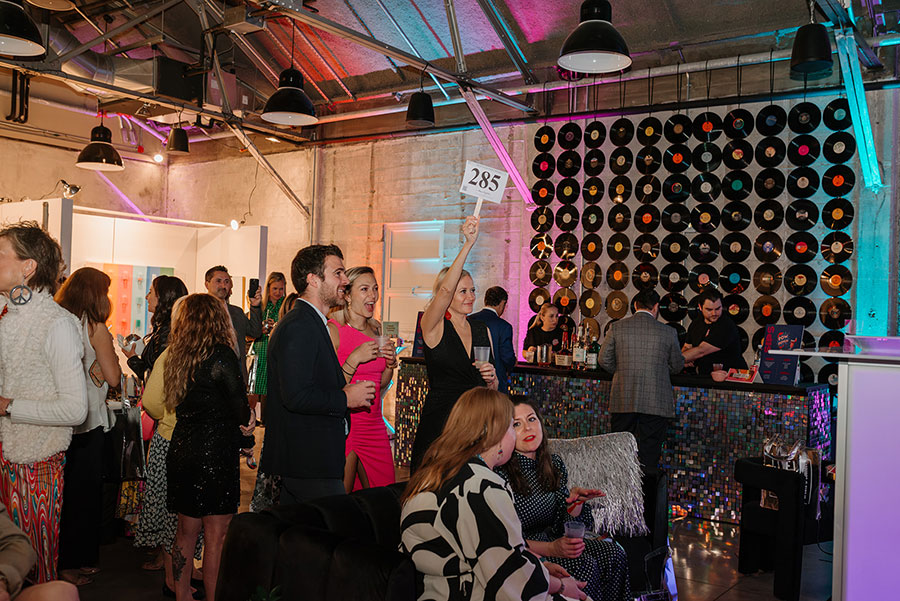 Guests mingling at a gala, surrounded by bright neon lights creating a vibrant atmosphere.